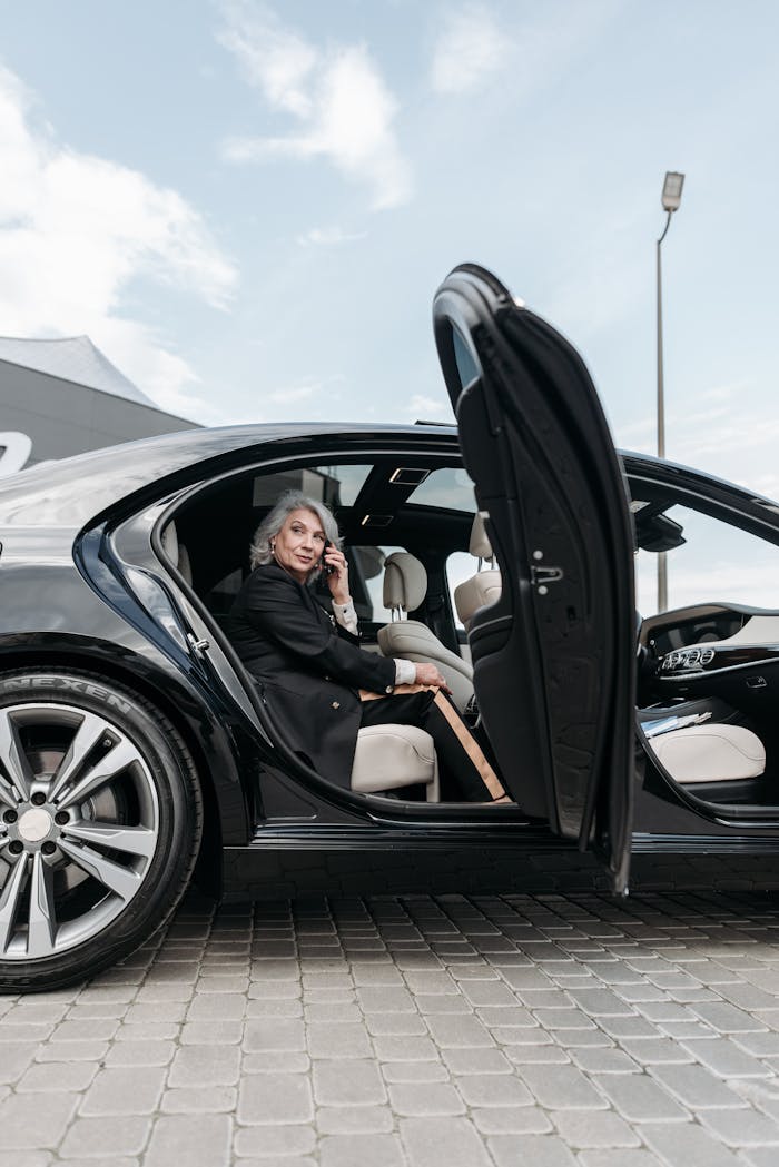 Confident senior woman sitting in a black luxury car, exuding elegance and success.